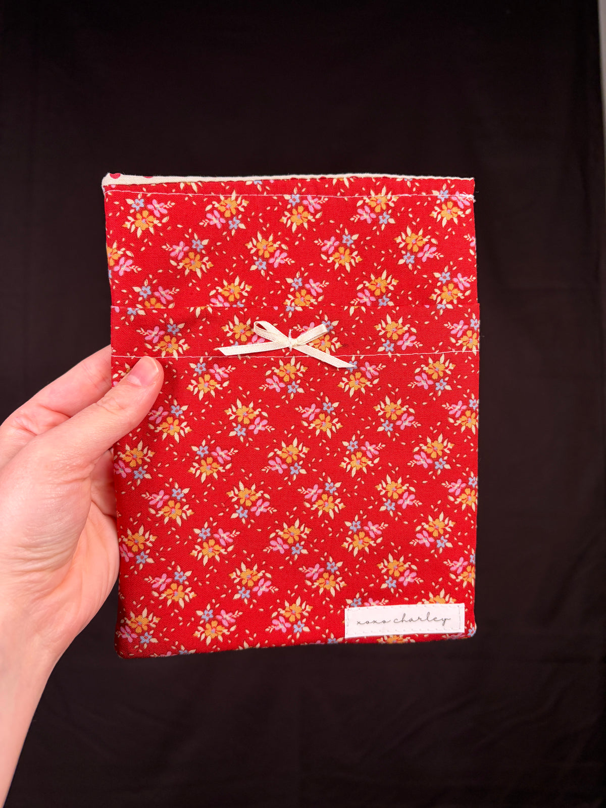 Red e-reader sleeve with frosted holly floral pattern, secured with white ribbon tie