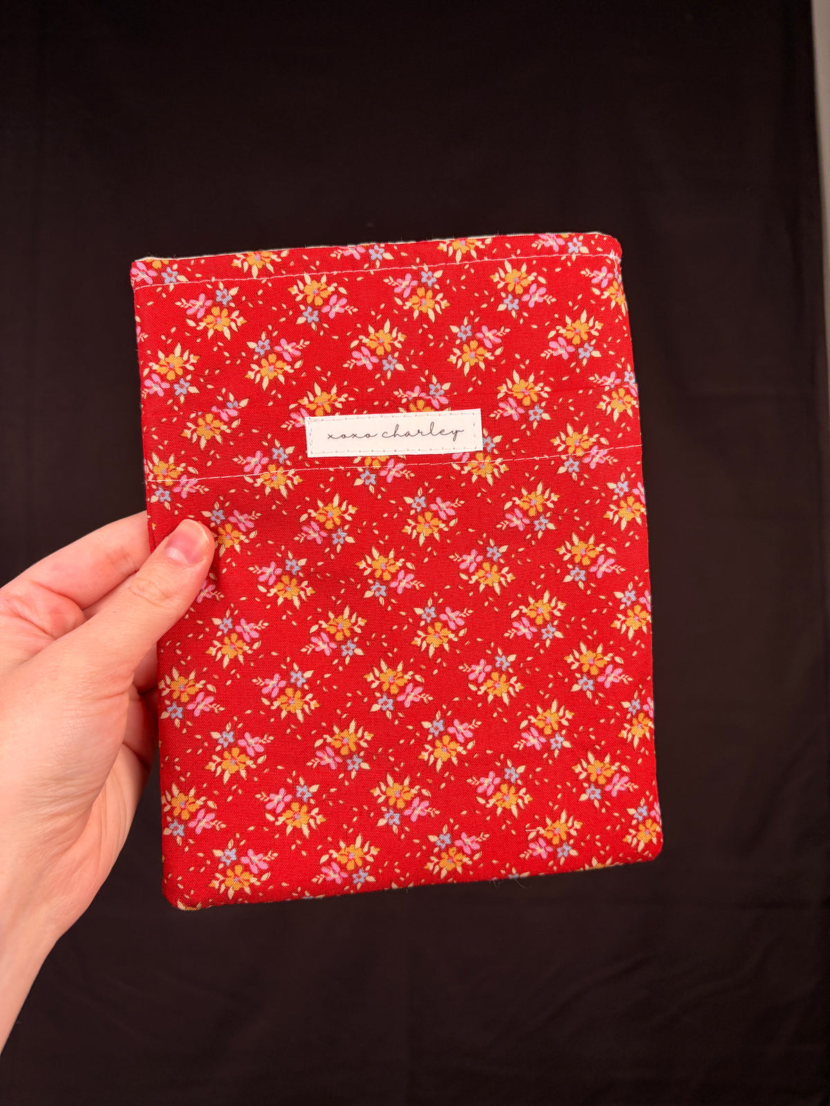 Red e-reader sleeve with floral pattern and small rectangular brand label