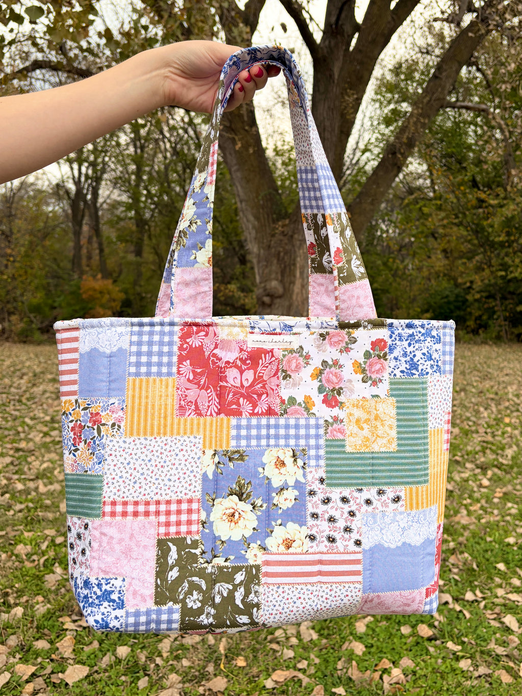 Patchwork picnic tote bag with pink, blue, and floral square panels and fabric handles