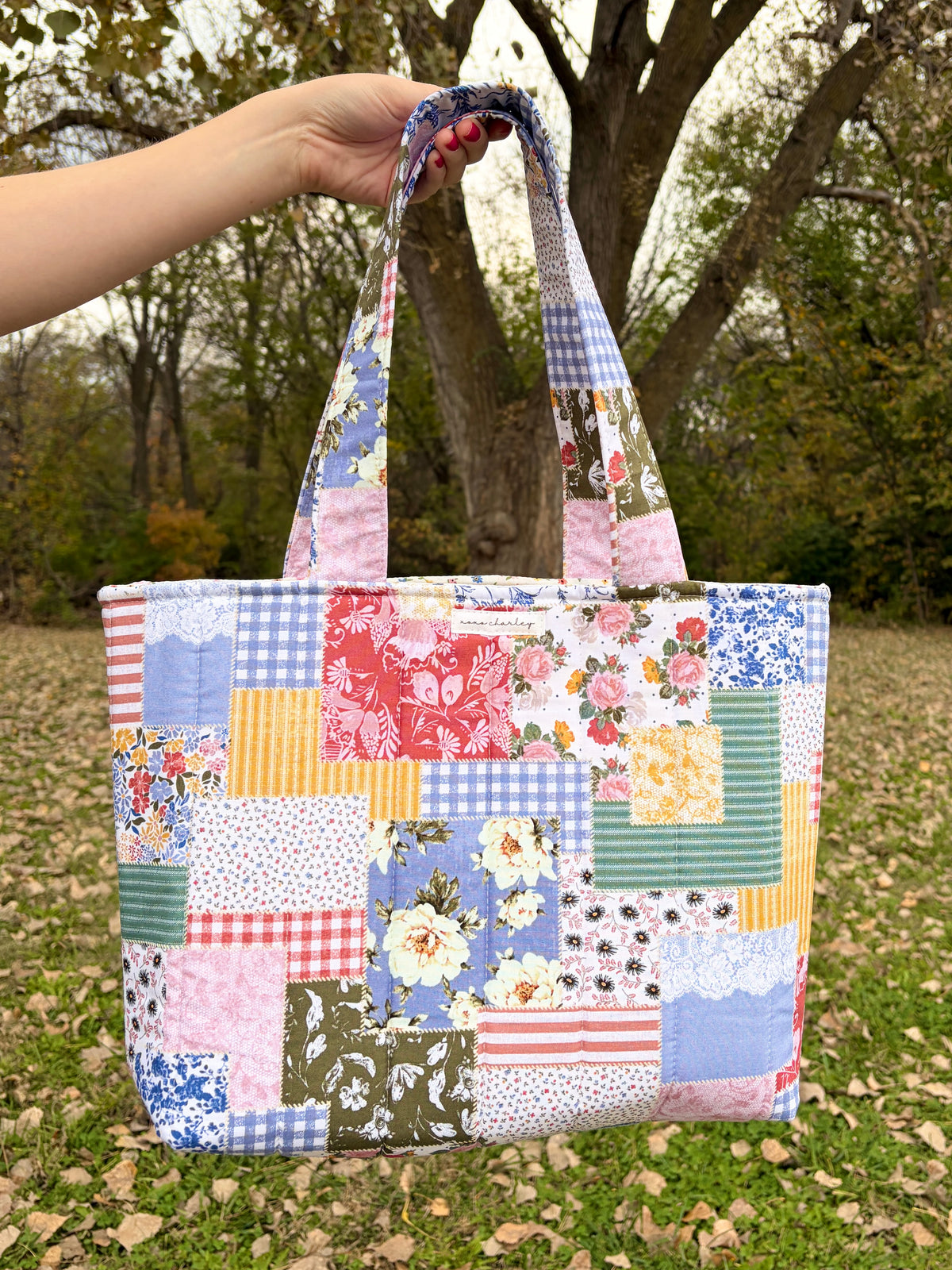 Patchwork picnic tote bag with pink, blue, and floral square panels and fabric handles
