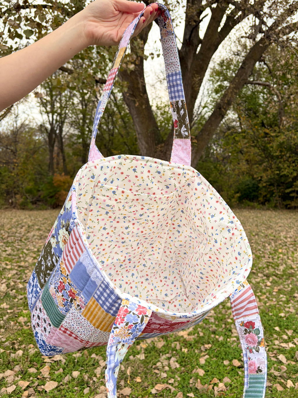 Patchwork tote bag held open, showing light interior lining and floral fabric handles