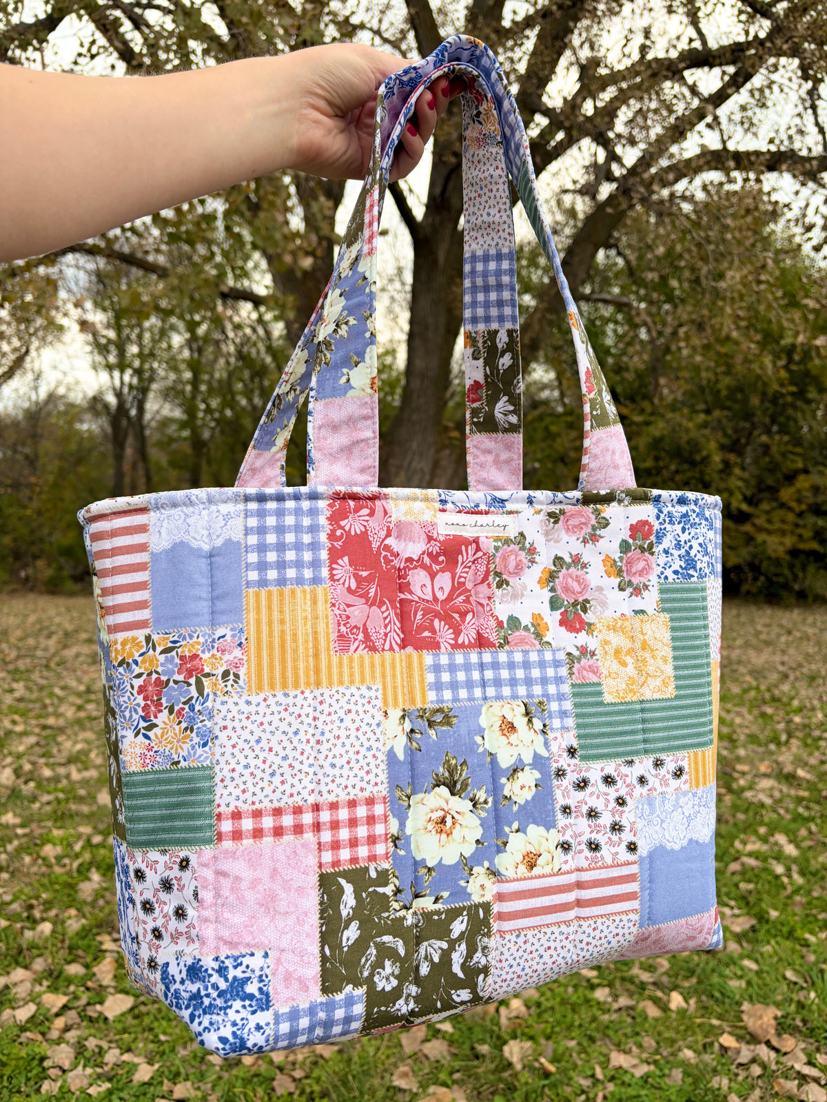 Patchwork picnic tote bag with colorful square panels, floral prints, and top handles