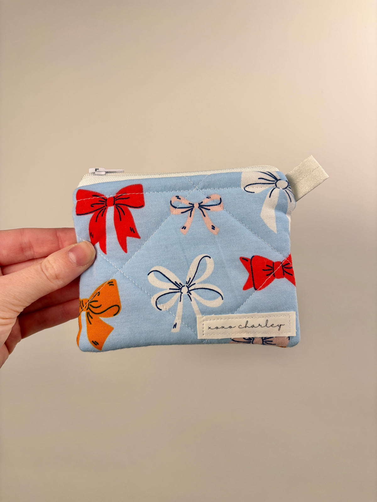 Blue zip pouch wallet with bow prints and light-colored zipper pull