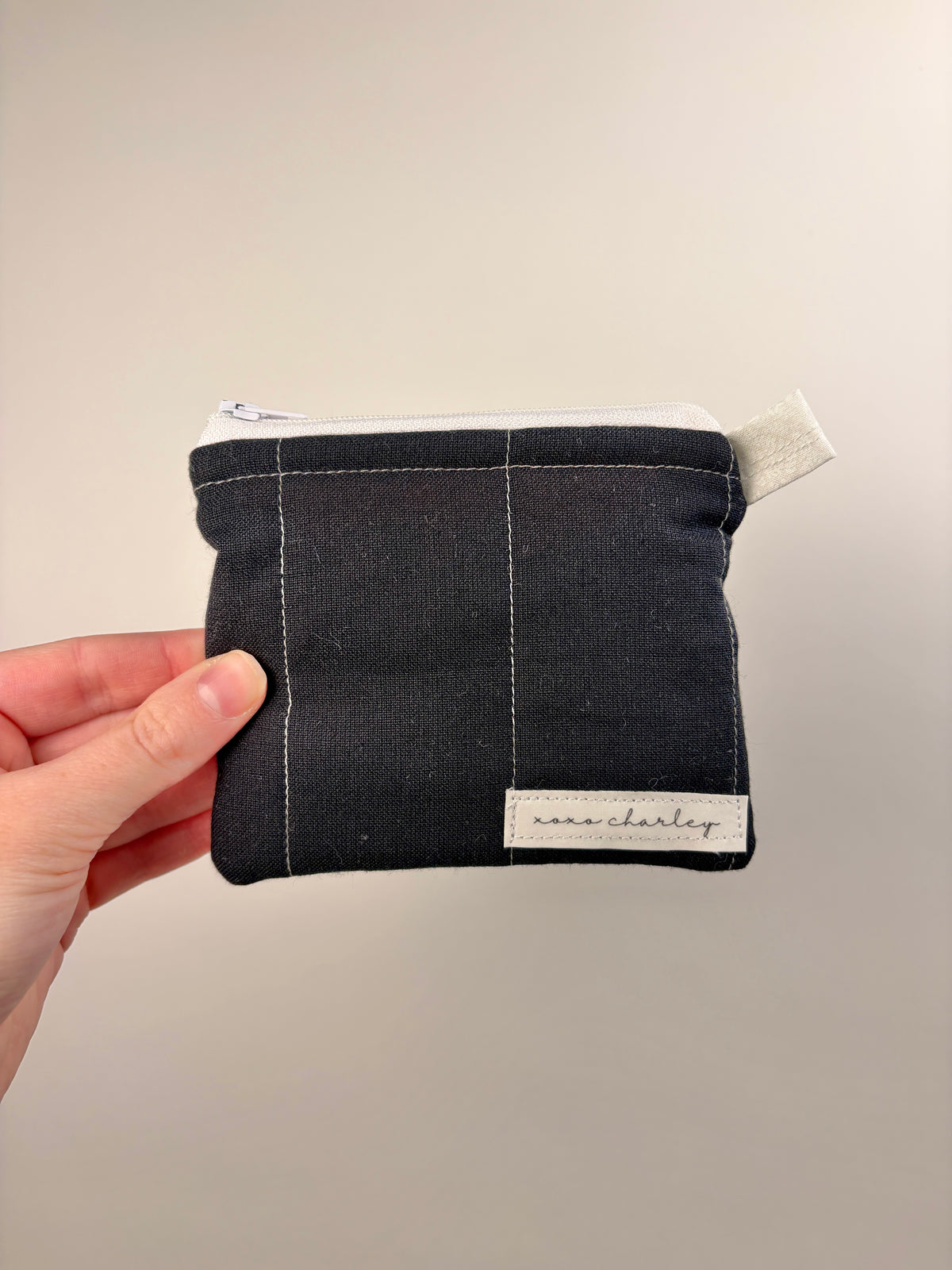 Dark fabric zip pouch wallet with stitched panel and brand label patch