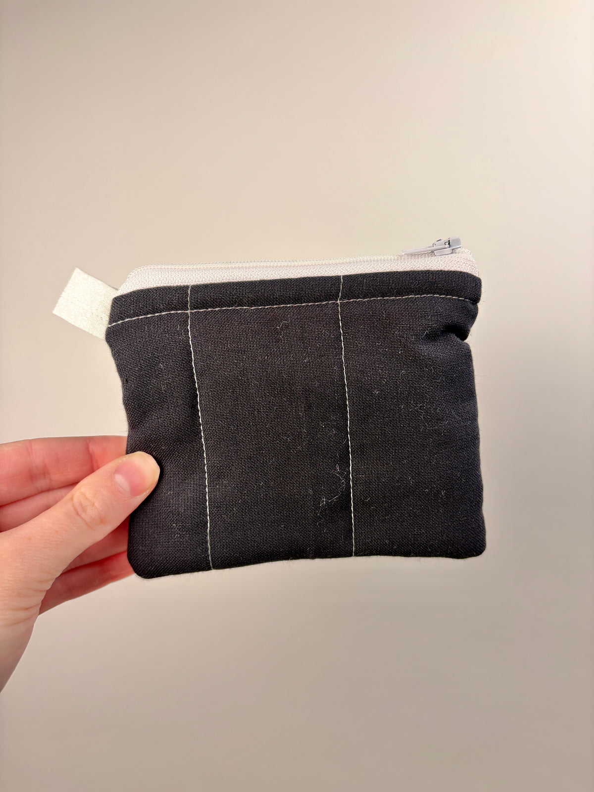 Dark fabric zip pouch wallet with stitched front panels and white lining trim