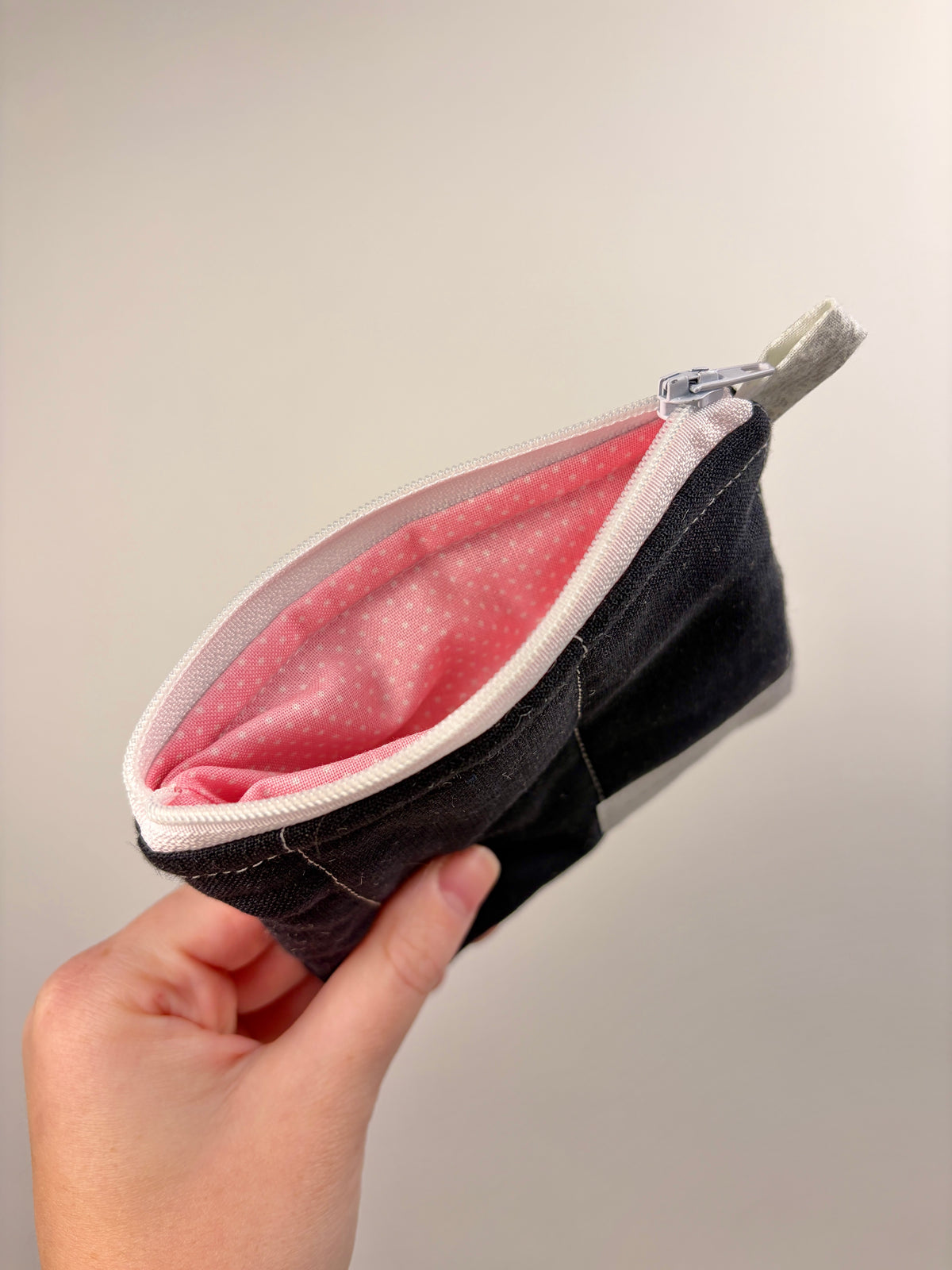 Open dark zip pouch wallet with pink polka-dot lining and white-trimmed zipper top