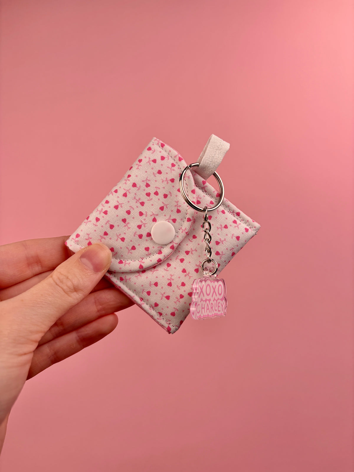 Pink heart-print earbuds case with snap flap and hanging XOXO Charley charm