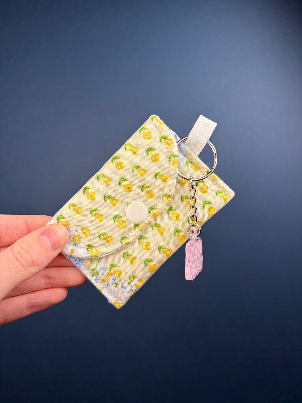 Patchwork earbuds case with yellow leaf print, blue floral trim, keyring and pink tag charm.
