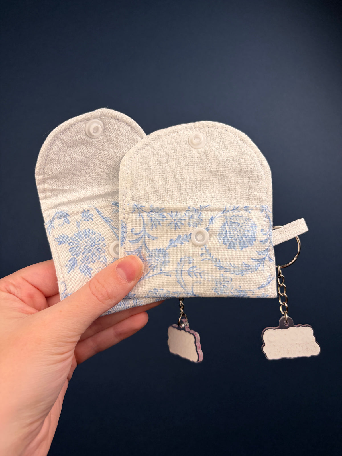 Pair of fabric pockets on blue floral earbuds case, with keyring and dangling charms