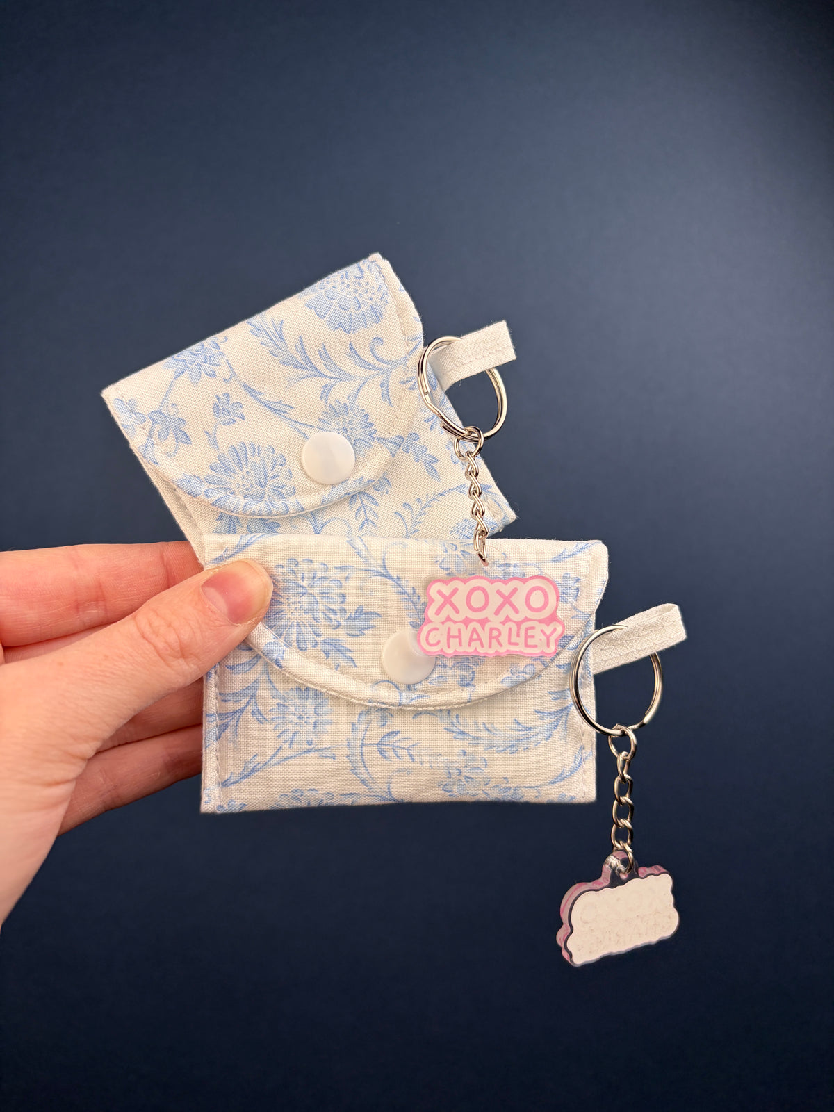 Blue floral earbuds case with snap closure and small keychain loop, with charm tags