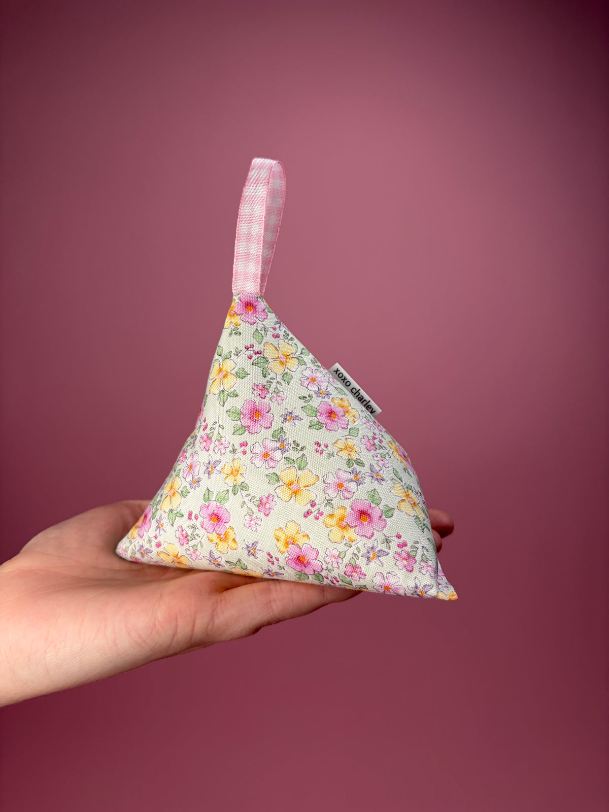 Floral fabric pyramid weight with pink ribbon, held at bottom