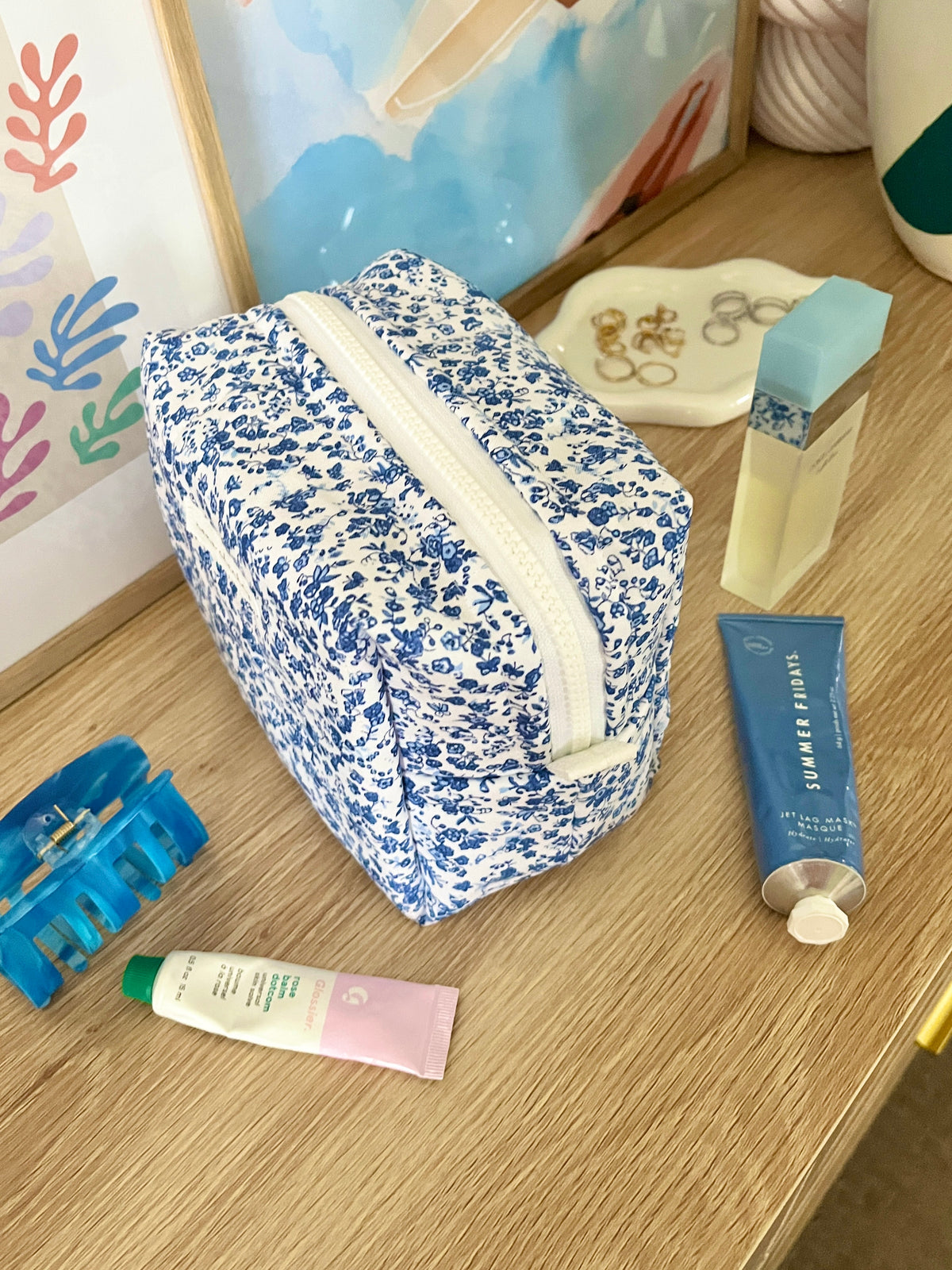 Medium makeup bag with blue floral print and cream strap, angled view