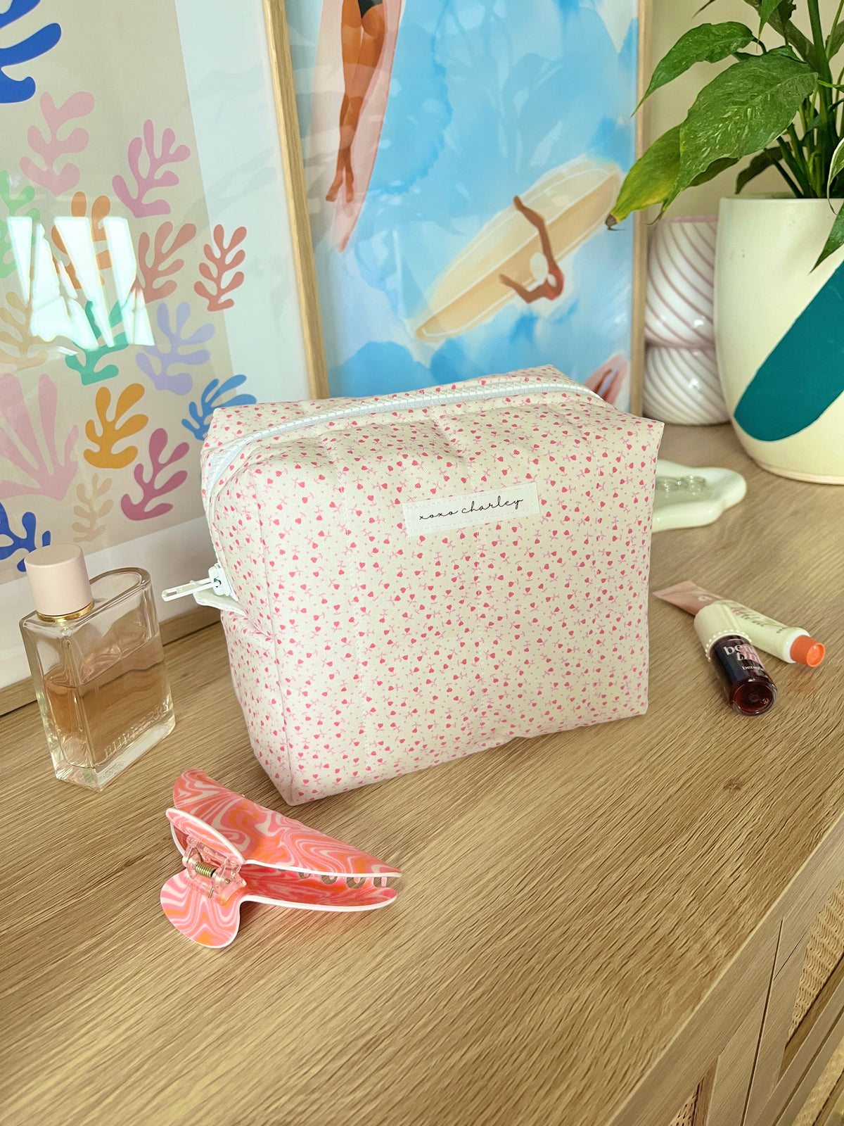 Pink medium makeup bag with tiny heart print, zip closure, and light blue trim.