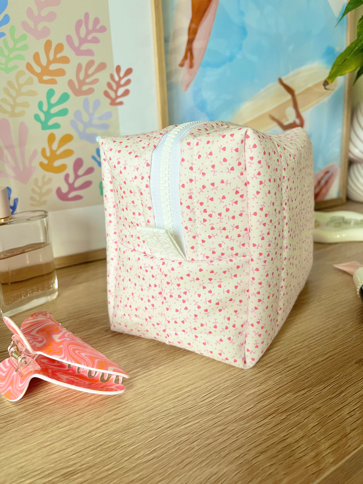 Pink heart-print medium makeup bag with light blue handle strap and zip-top.