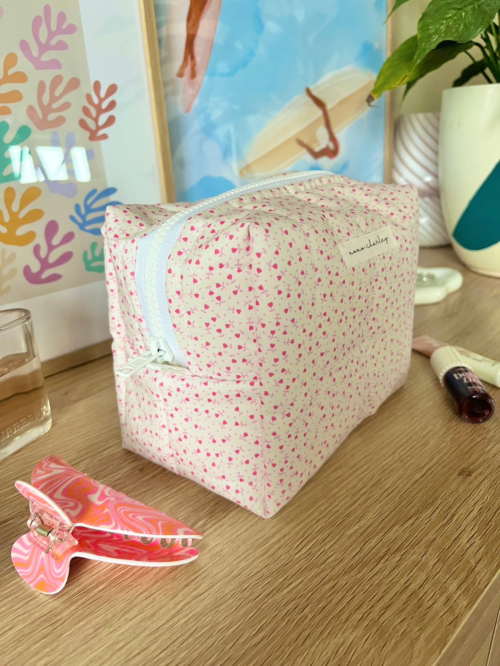 Pink medium makeup bag with tiny heart pattern, zip-top and light blue contrast trim.