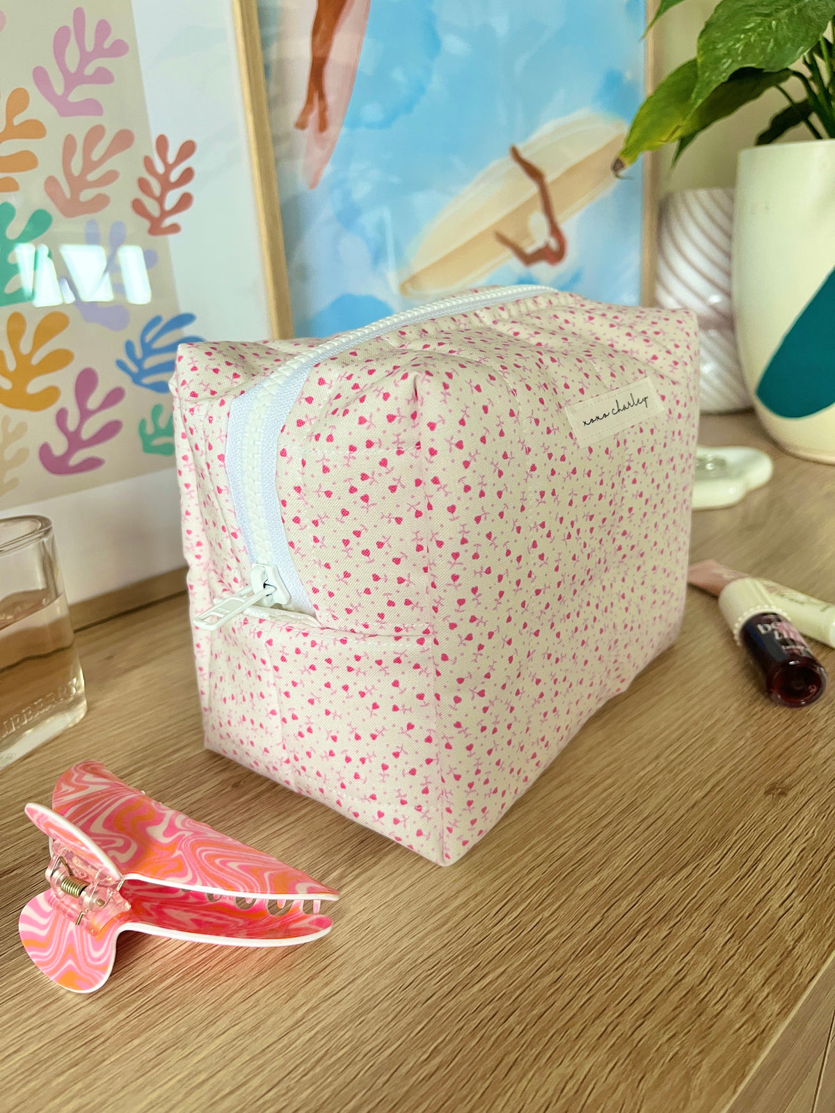 Pink medium makeup bag with tiny heart pattern, zip-top and light blue contrast trim.