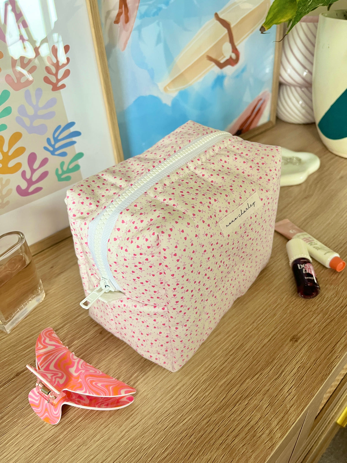 Pink heart-print makeup bag, medium size, zip closure and light blue edging detail.