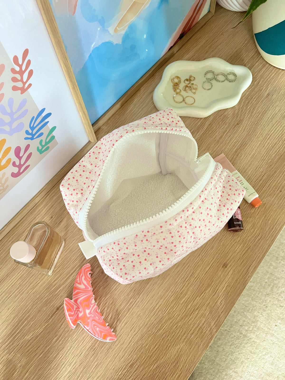 Open medium makeup bag in pink tiny heart print with white lining and zip-top opening.