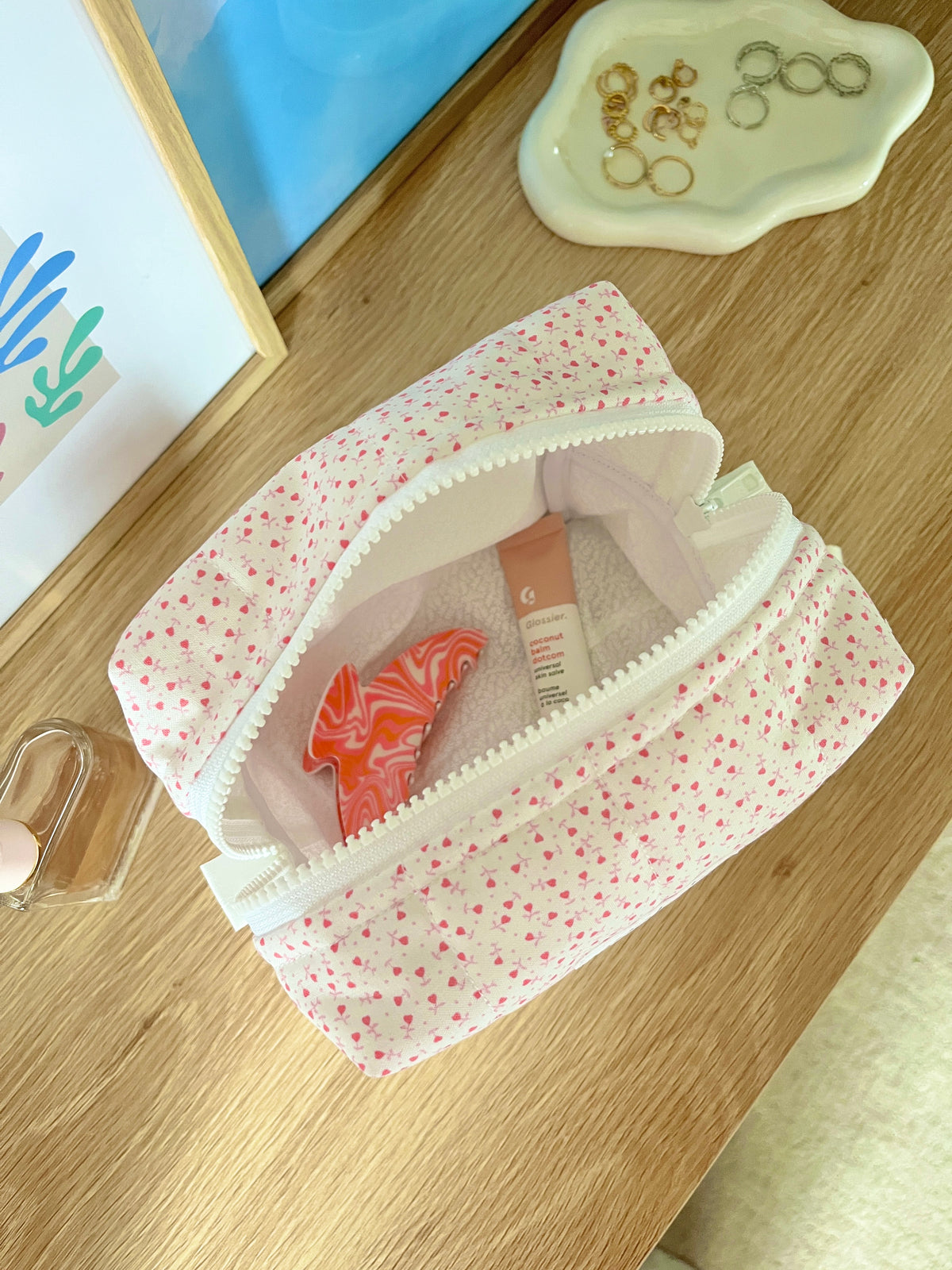 Open pink heart-print medium makeup bag with white interior and contents partially visible.