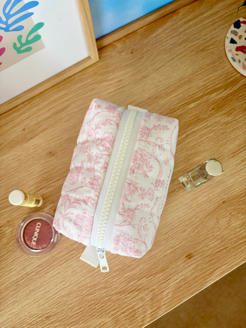 Pink floral mini makeup bag lying down with top zipper and strap