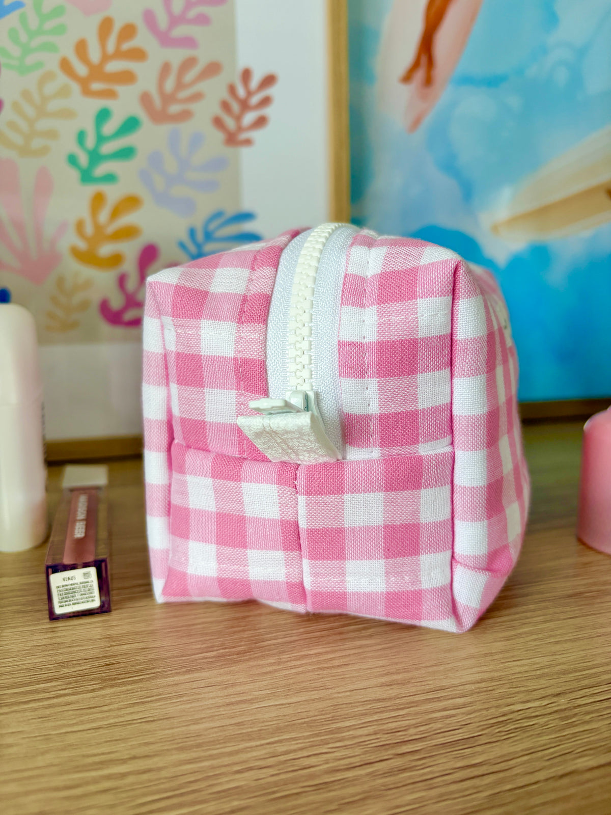 Pink gingham mini makeup bag with white zipper and top handle loop.