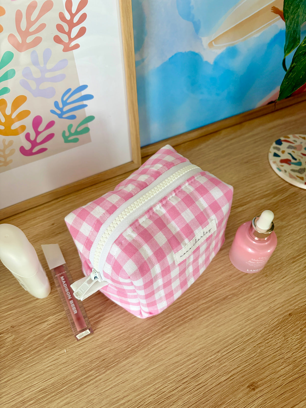 Pink gingham mini makeup bag with white piping and zippered top opening.