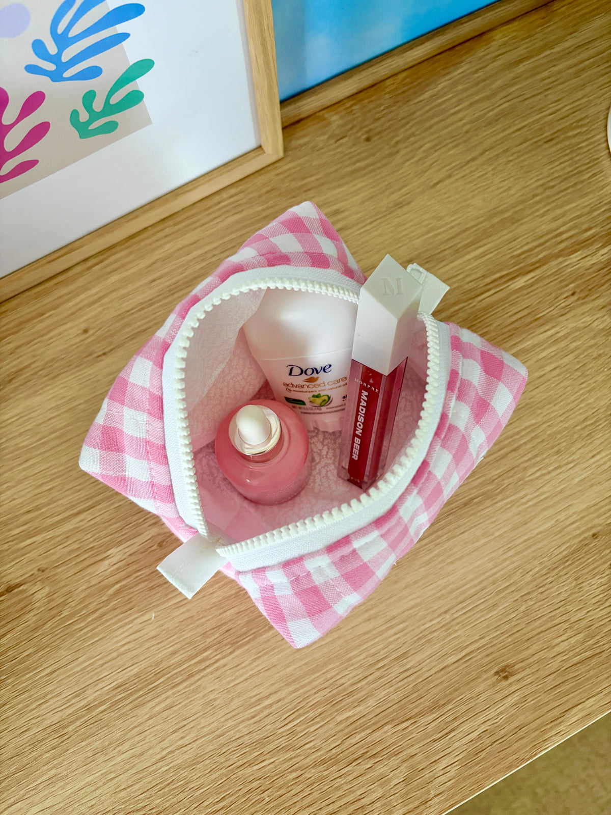 Pink gingham mini makeup bag with open lined interior and visible white zipper pull.