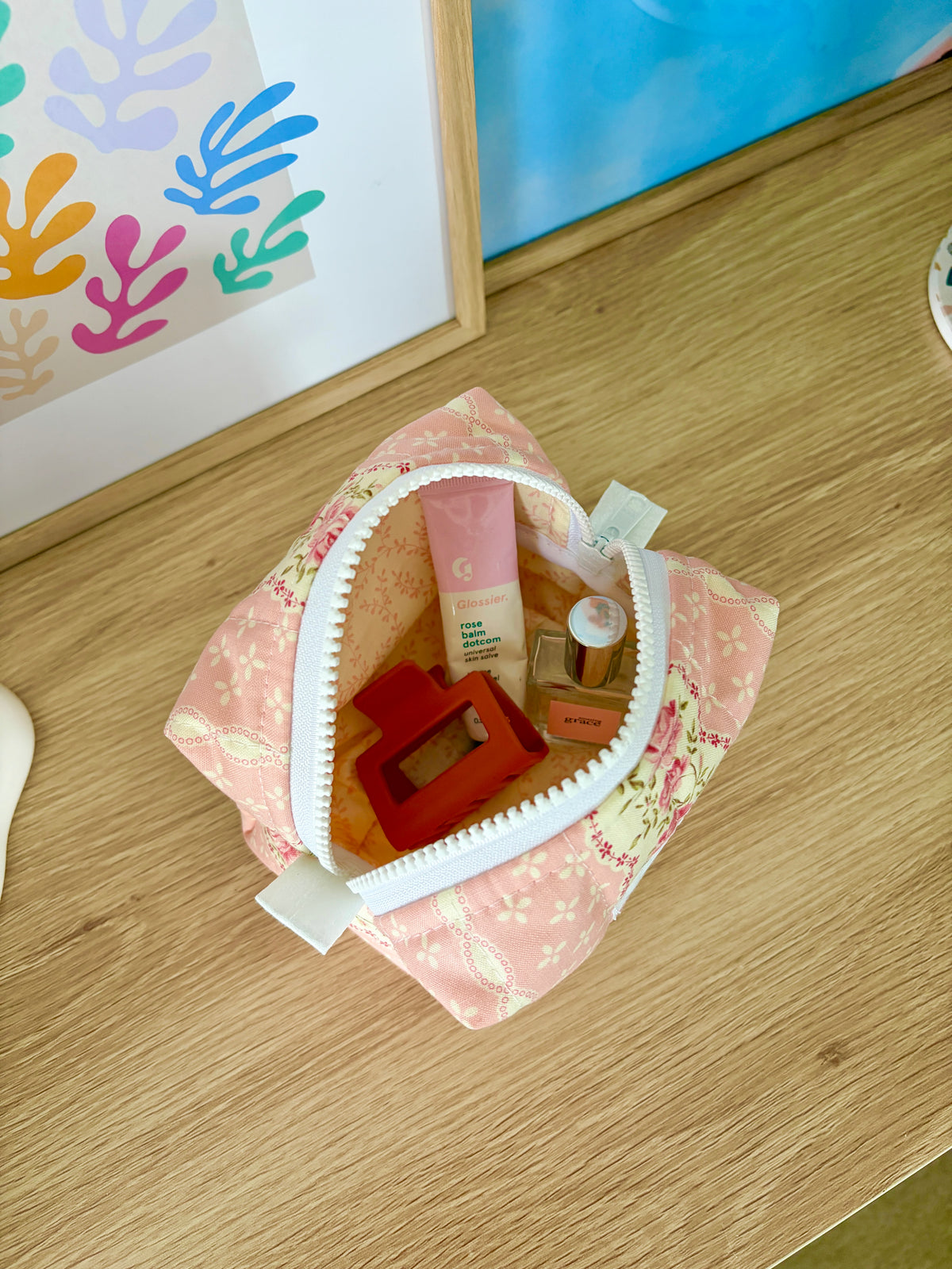 Open pink floral mini makeup bag with white zipper trim and interior items