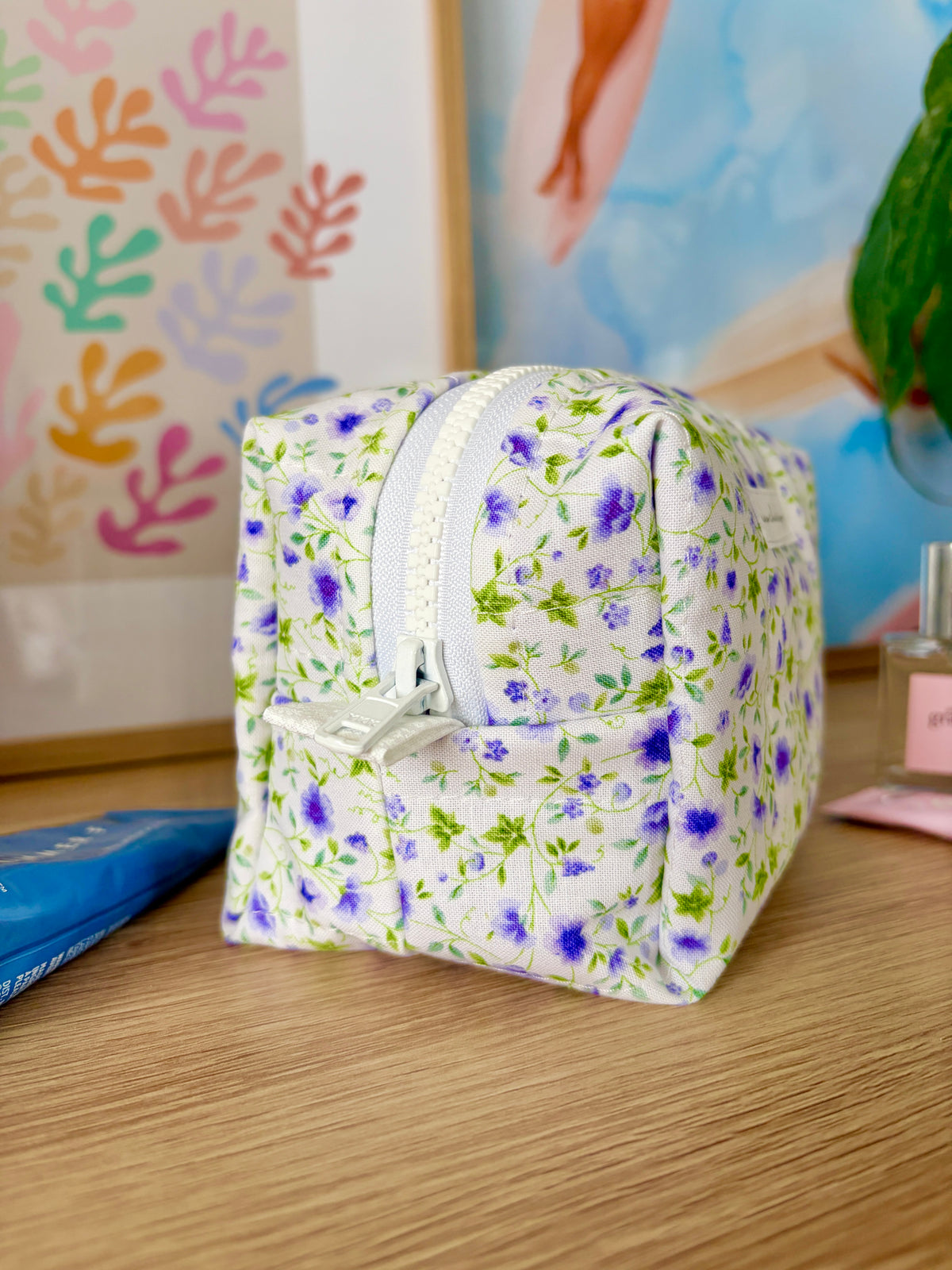 Mini floral makeup bag with zip; white base with purple floral print and rounded shape