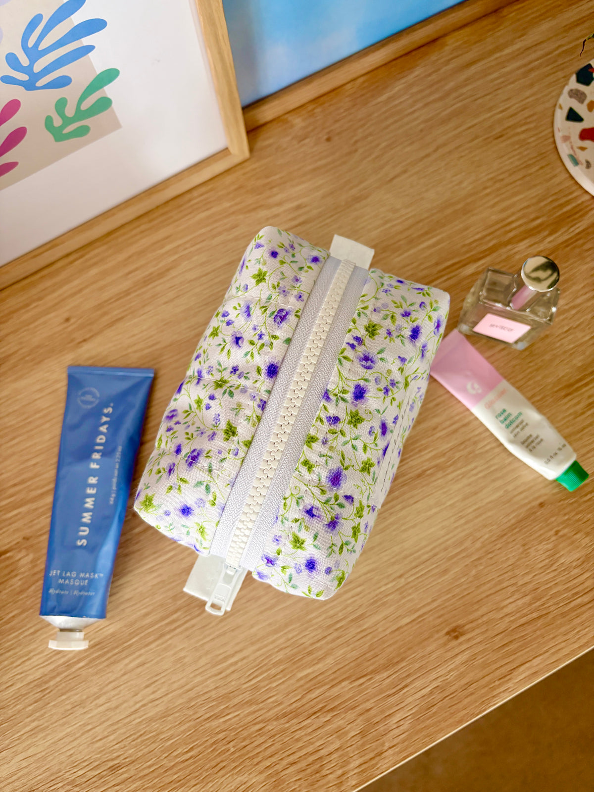 Mini floral makeup bag, zippered pouch in white with purple flower pattern; side view