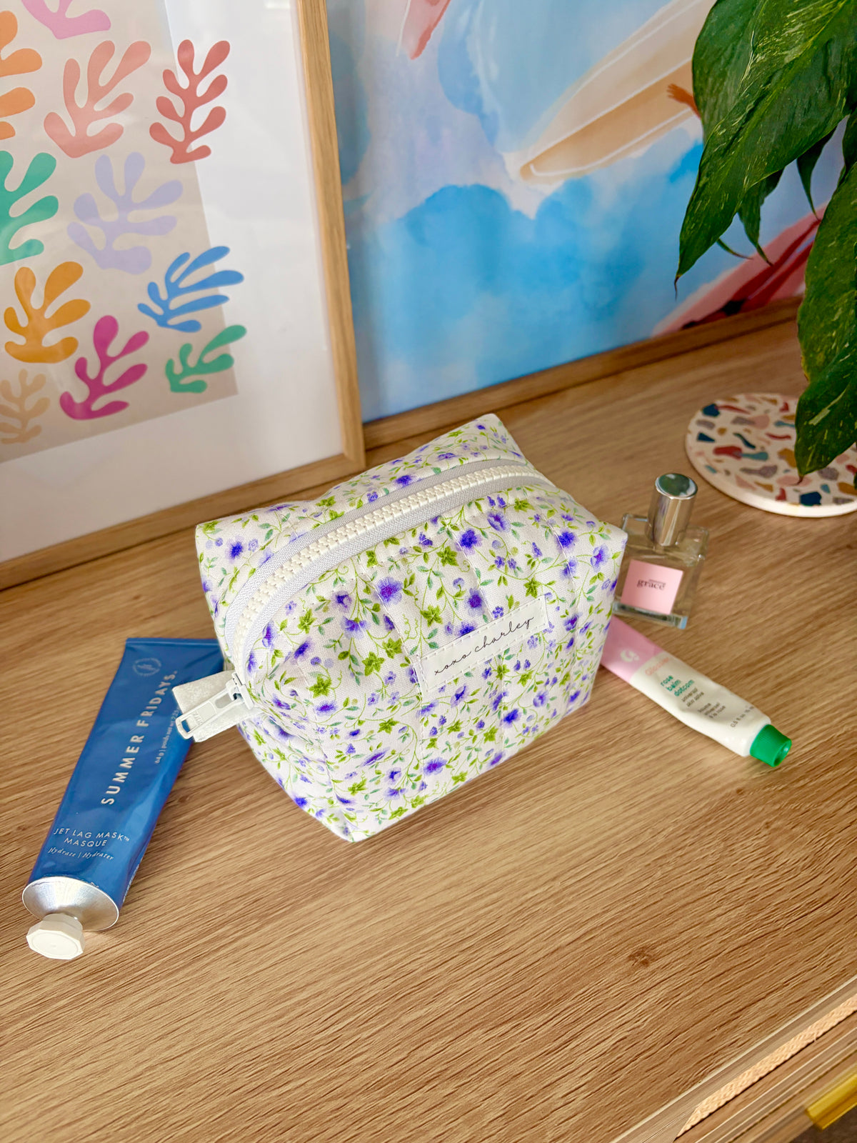 Mini floral makeup bag on table, white with purple and green floral print; zip detail