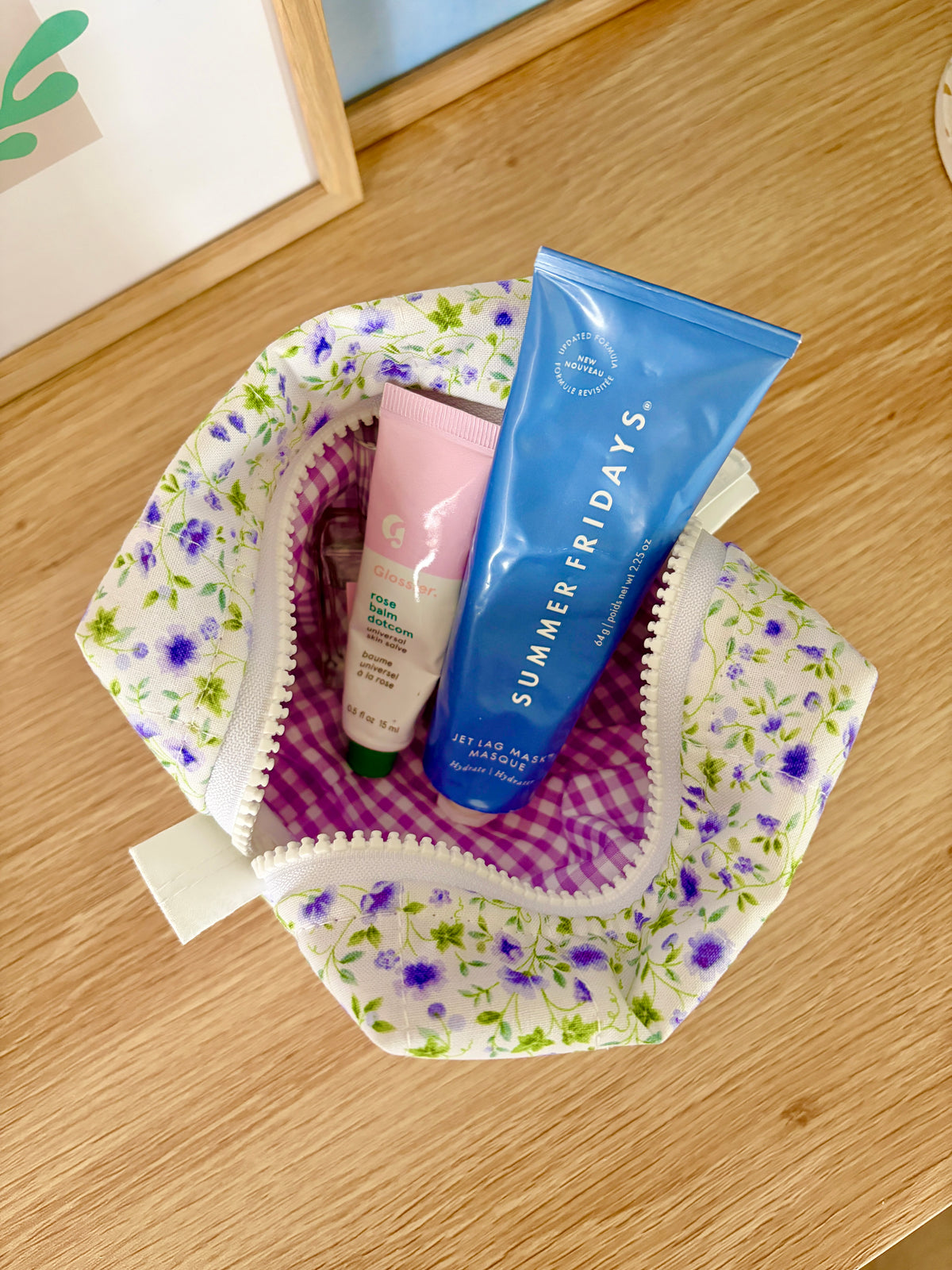 Open mini floral makeup bag with purple gingham lining and stacked toiletries inside