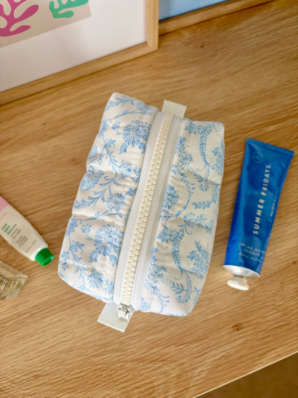 Vintage blue mini makeup bag with white top zipper on blue floral fabric, angled view.