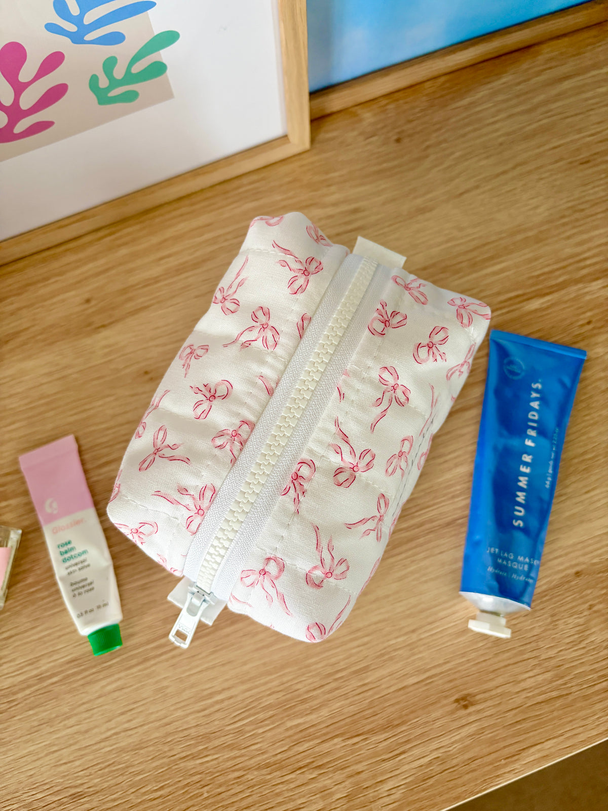 Mini makeup bag with pink bow print, open zip track and curved top edge