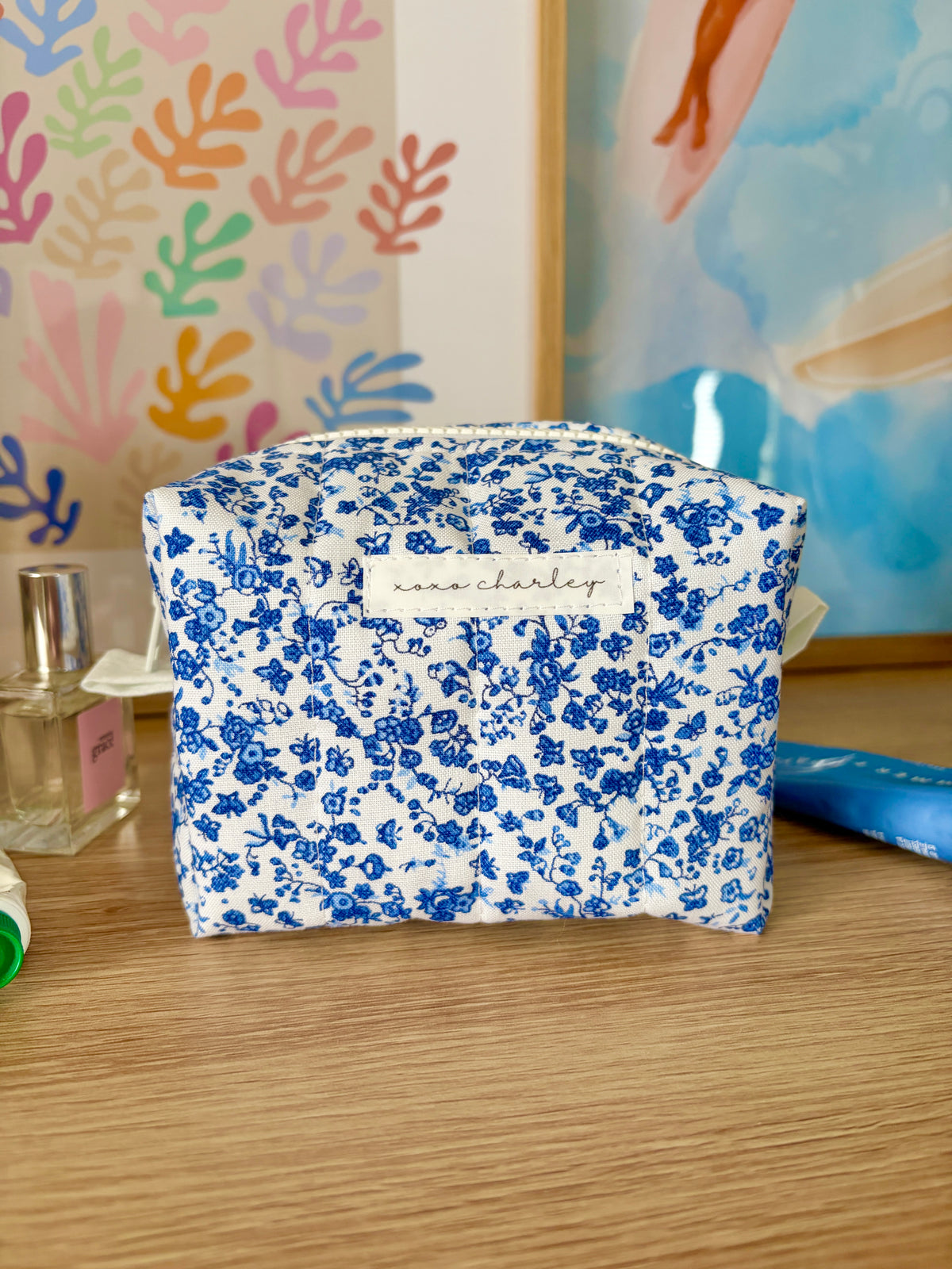 Mini makeup bag in blue with white floral pattern, top zip closure.