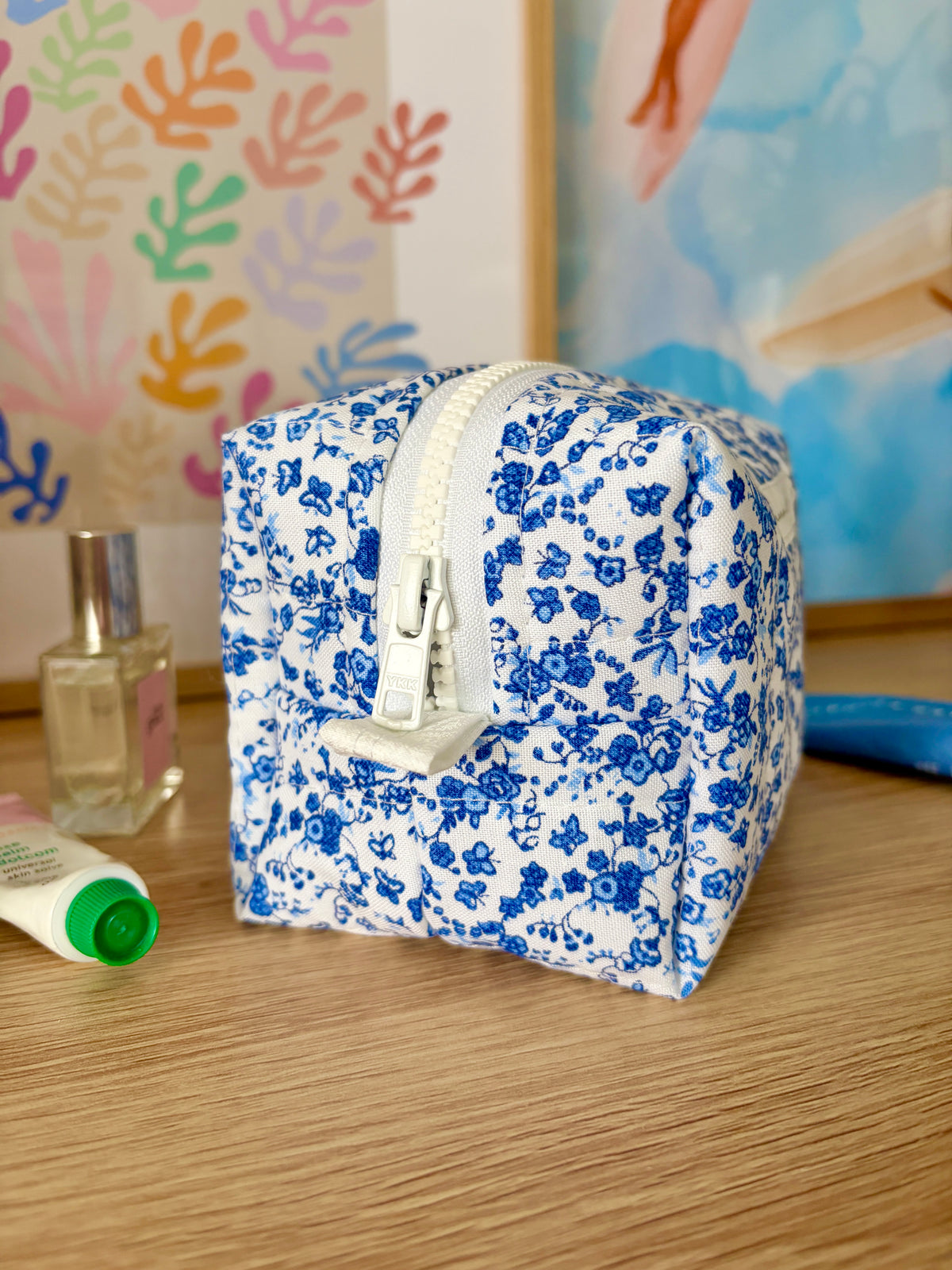 Blue floral mini makeup bag with front zipper and small side handle tab.