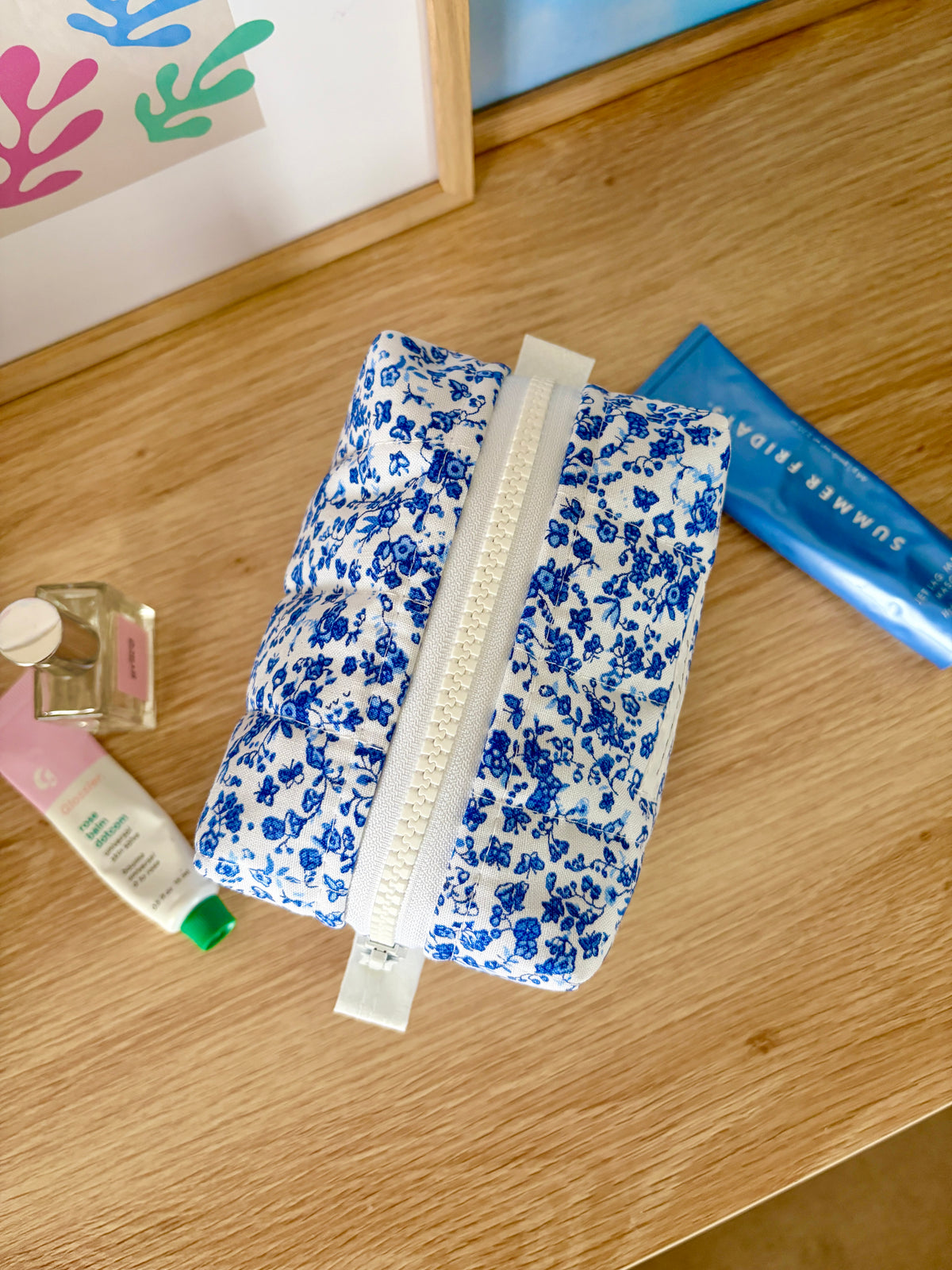Blue floral mini makeup bag opened, showing white zipper and fabric lining.