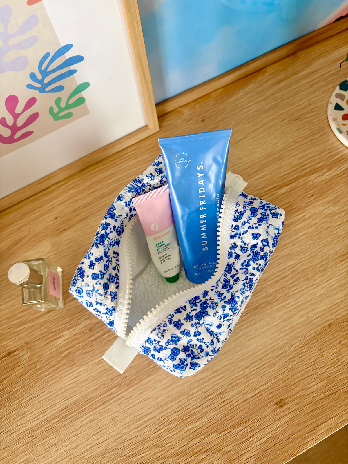 Blue floral mini makeup bag filled with skincare tubes, zip top open.