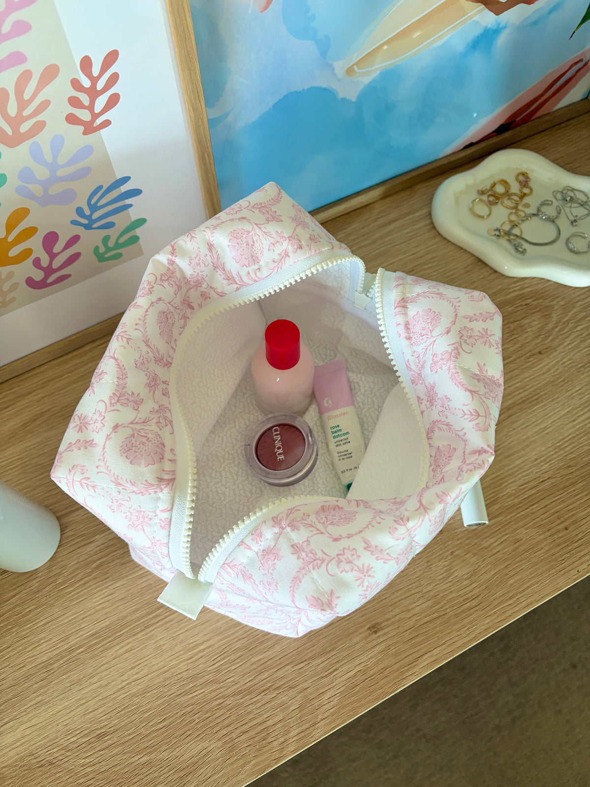 Large pink patterned makeup bag open, holding small bottles and compact