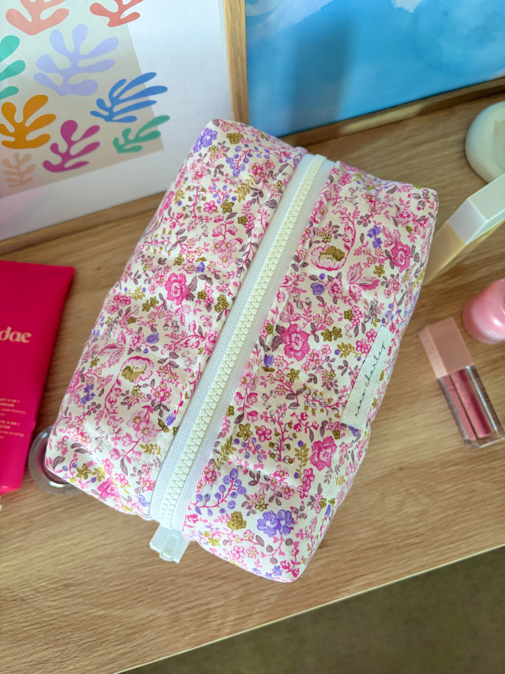 Pink floral large makeup bag leaning sideways, white zipper detailing visible.