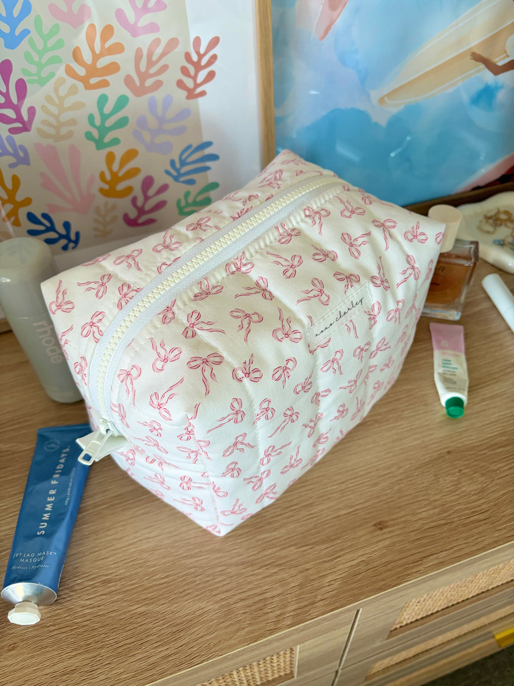 Pink bow-print makeup bag with white zipper and small top handle tab