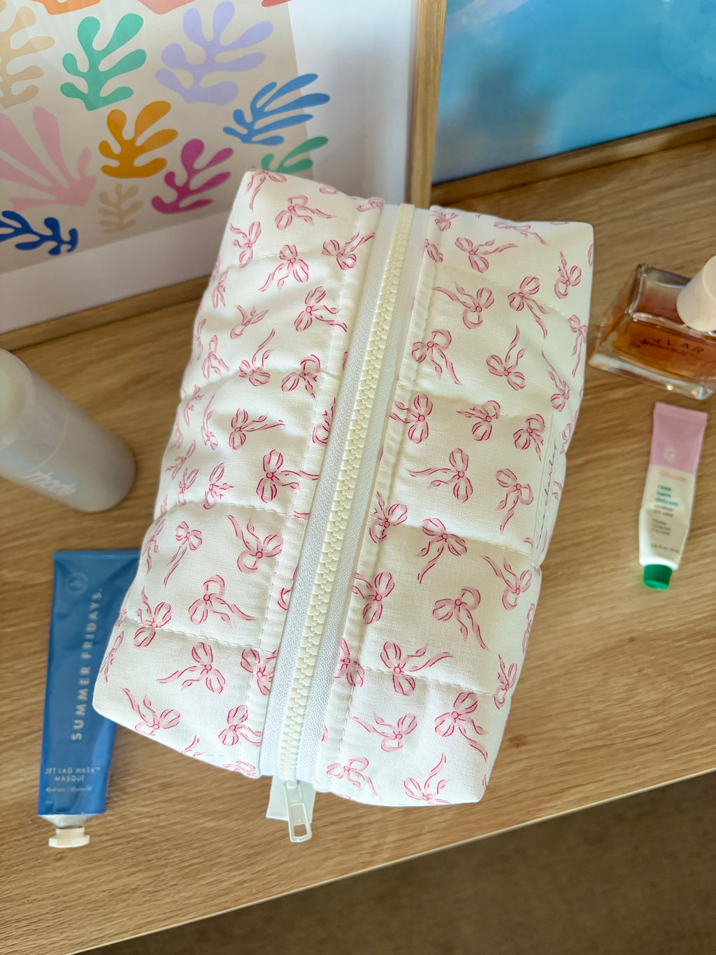 Pink bow-print makeup bag with long vertical zipper and hanging pull tab