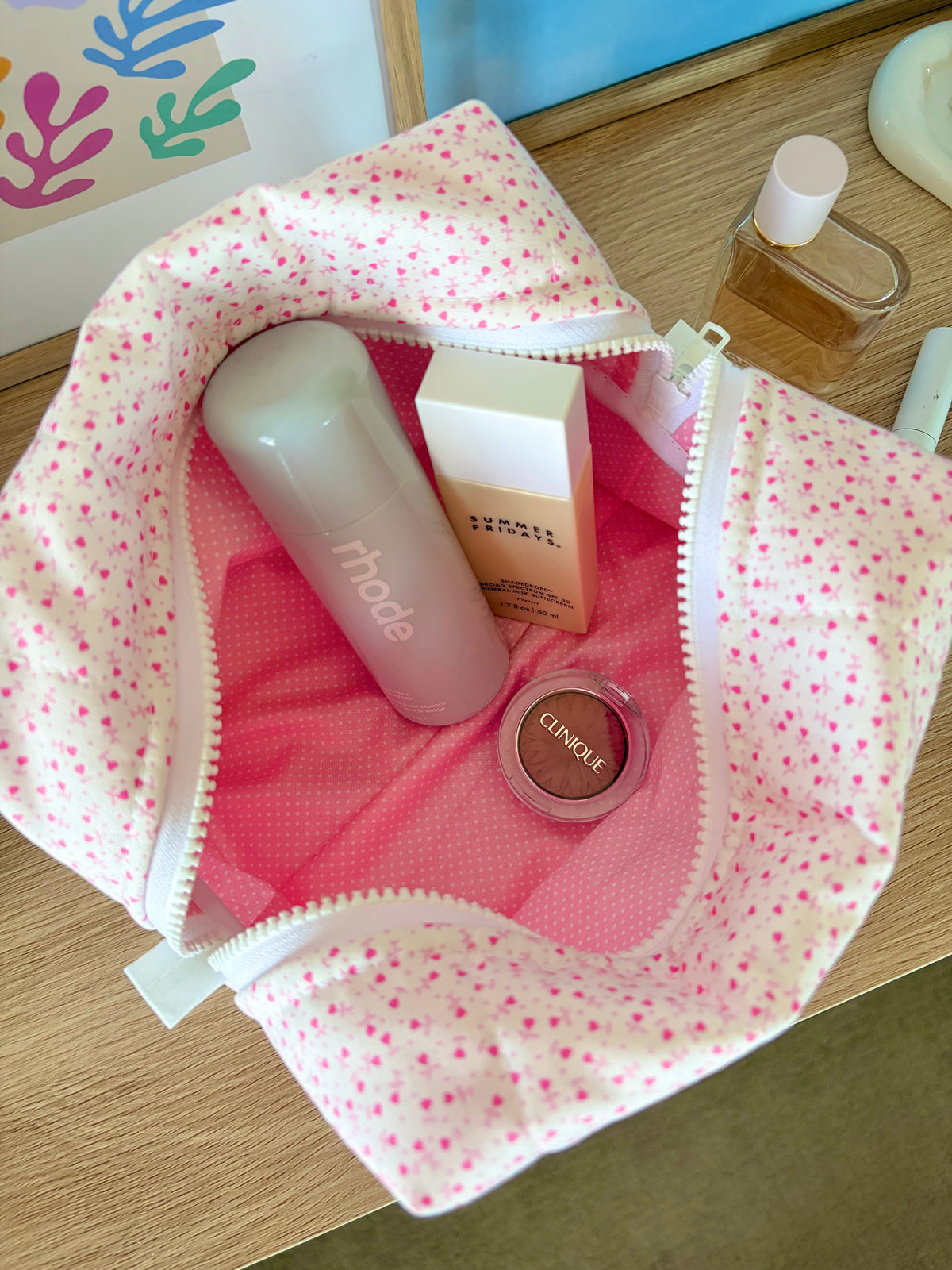 Large open pink makeup bag with tiny heart print, holding lip balm, box, compact