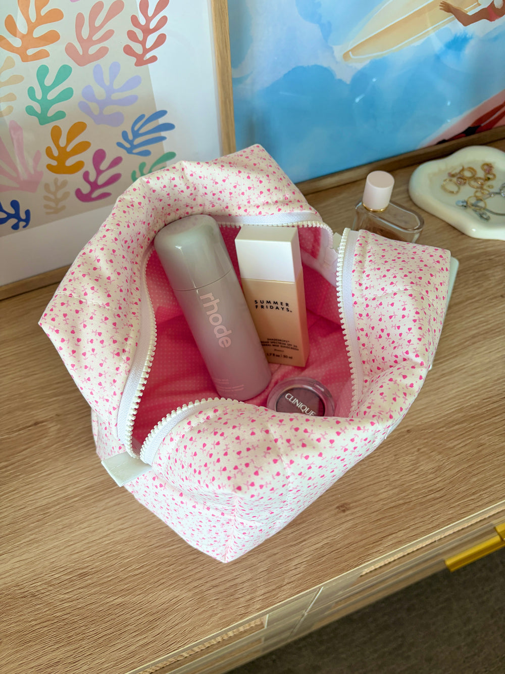 Large open pink makeup bag with tiny heart print, showing cosmetics and round compact