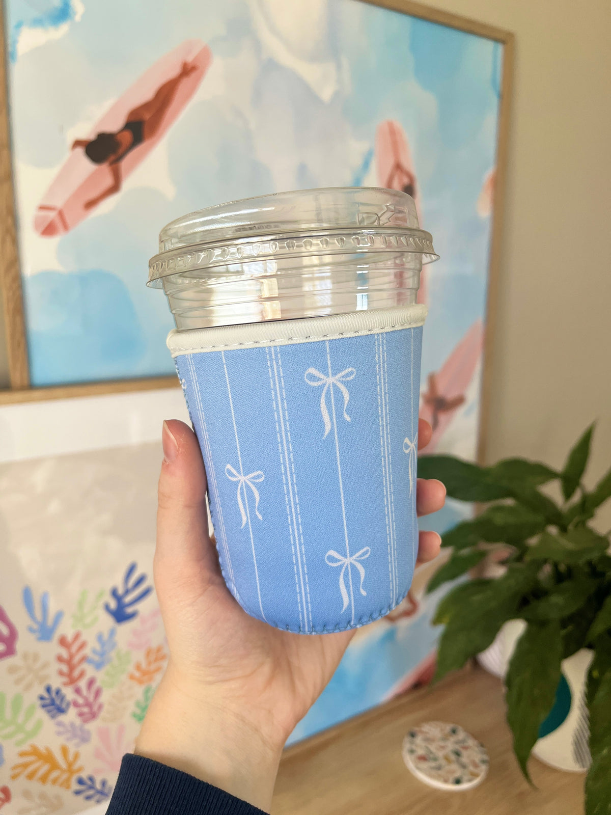 Blue cup sleeve with vertical stitching and small bow icons on the front.