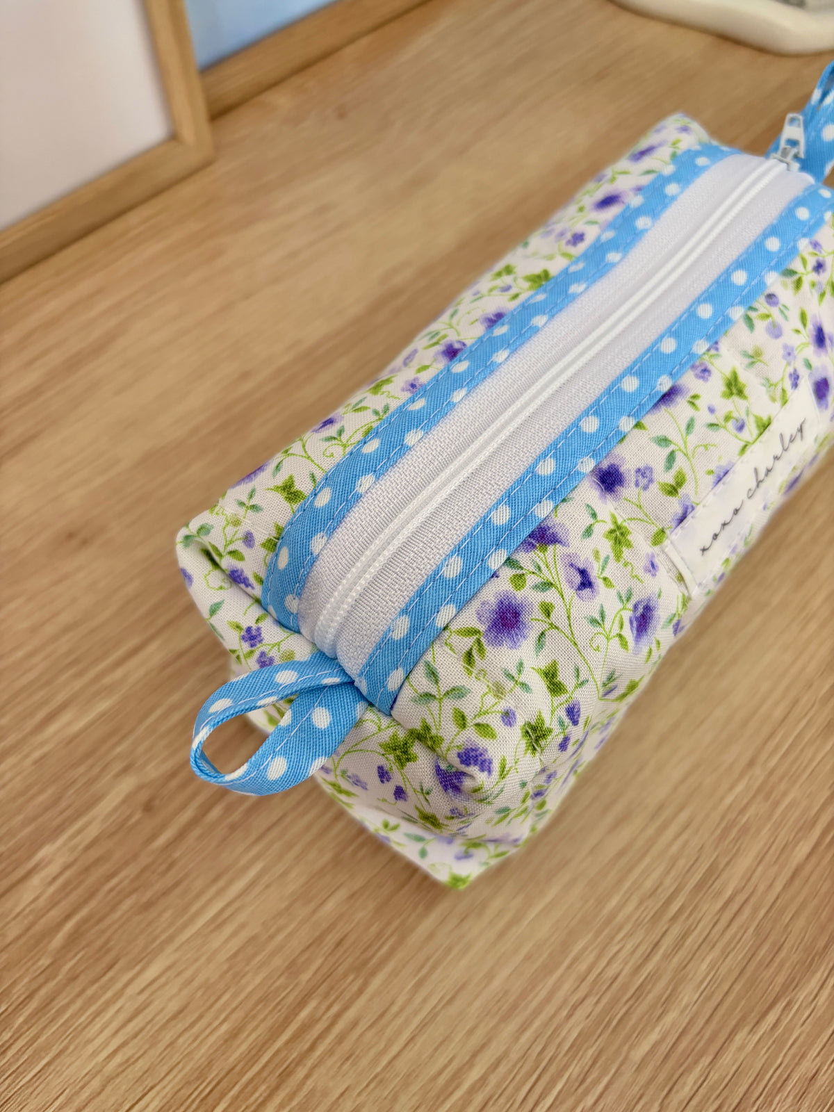 Floral fabric pouch with blue zipper stripe and ribbon loop handle