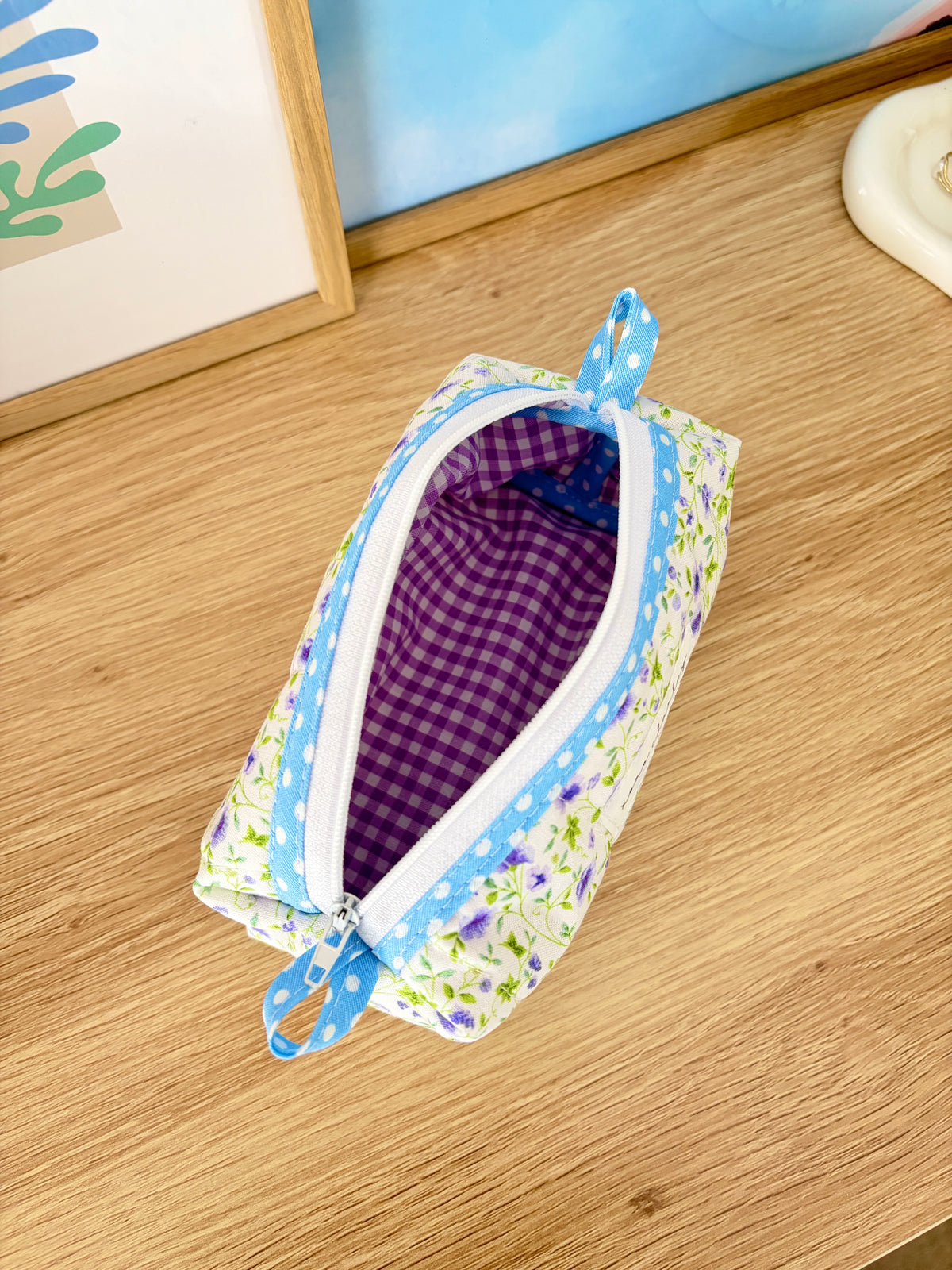 Floral fabric pouch open to purple gingham interior with blue ribbon zipper tab
