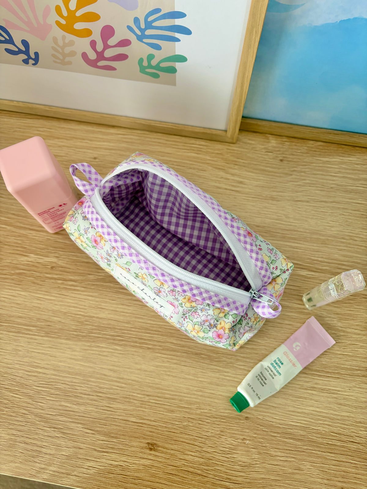 Floral zip pouch bag open to purple gingham interior, with top zipper and bow