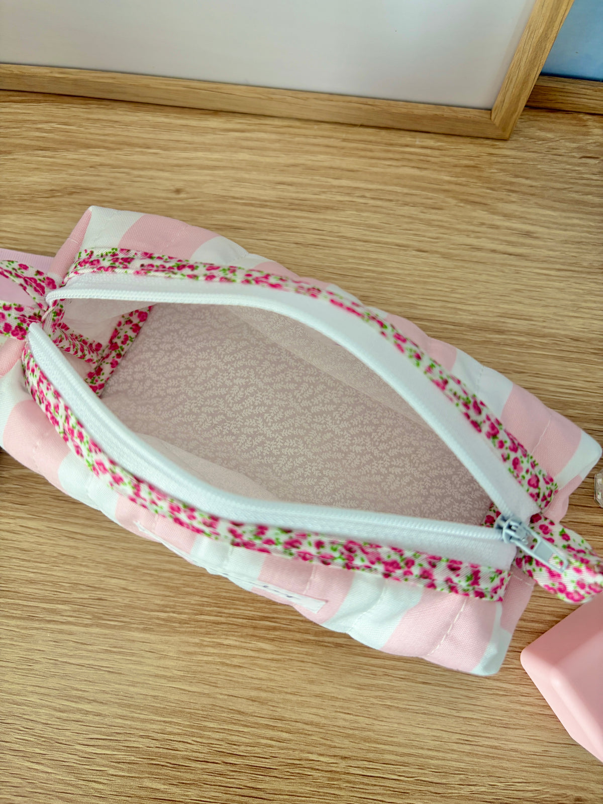 Close-up top view of pink and white striped zip pouch bag with floral trim and textured lining