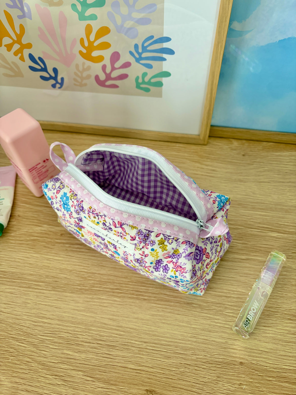 Purple floral zipper bag with opening showing purple gingham lining and light pink handle